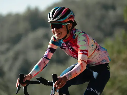 Ricarda Bauernfeind lacht auf ihrem Rennrad, trägt einen bunten Helm und ein auffälliges Trikot mit geometrischen Mustern.