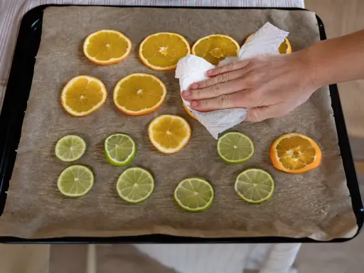 En hand torkar apelsinskivor på en plåt med bakplåtspapper. Citrusfrukter förbereds för att torka.