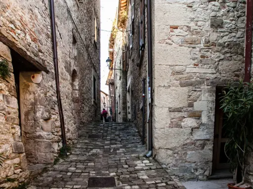Un vicolo acciottolato a Pennabilli, Rimini, con antiche case in pietra e una persona con un cappotto rosa.