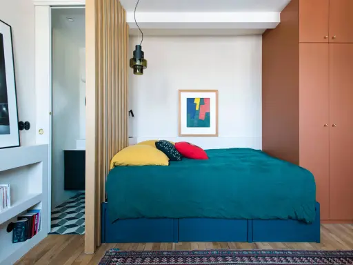 Une chambre cabine cosy avec un lit bleu canard, des coussins colorés et une armoire ocre. Un paravent en bois sépare l'espace nuit de la salle de bain.