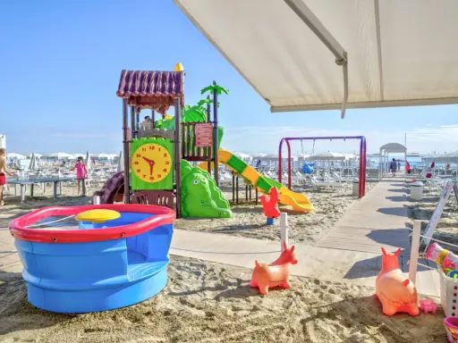 Area giochi su sabbia con scivolo, altalena e giochi d'acqua, un vero lido per bambini.