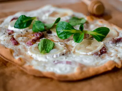 Tarte flambée alsacienne garnie de lardons, fromage de chèvre et jeunes pousses.