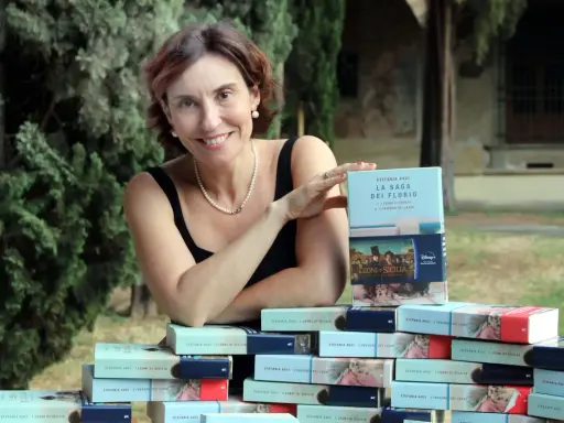 Stefania Auci sorride, circondata dai suoi libri "I Leoni di Sicilia" e "L'inverno dei leoni", celebrando il successo della saga.