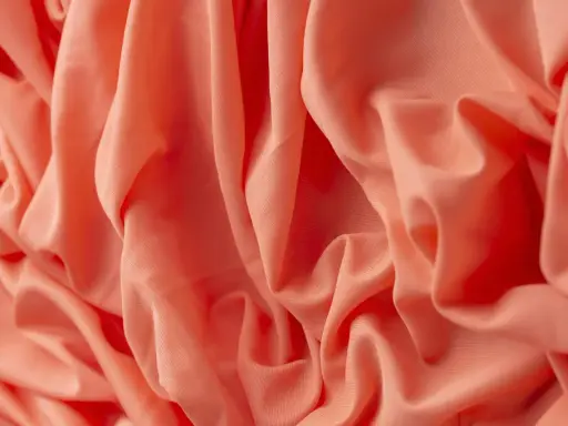 Tessuto arancione con pieghe morbide. Il materiale acrilico, cos'è? Una fibra sintetica versatile e resistente, ideale per abbigliamento e tessuti d'arredo.
