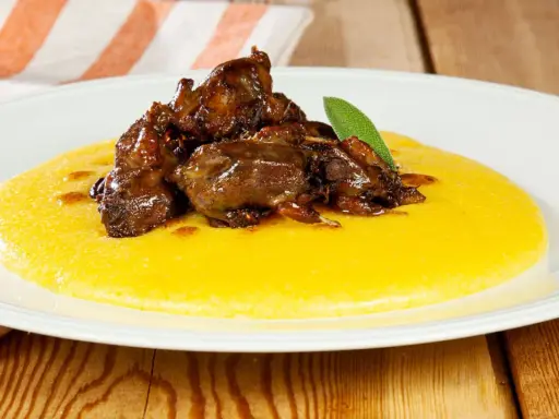 Piatto di polenta e osei, con uccellini scuri in umido e una foglia di salvia.