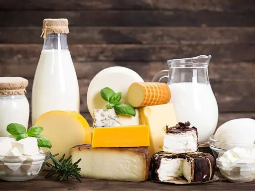 Milchprodukte wie Käse und Milch, die Laktose enthalten, sind auf einem Holztisch arrangiert.