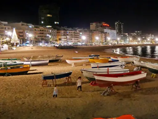 Boote am Strand bei Nacht, beleuchtete Stadt und Weihnachtsbaum. Selbst im Spanien Winter ist die Temperatur angenehm für einen Spaziergang.