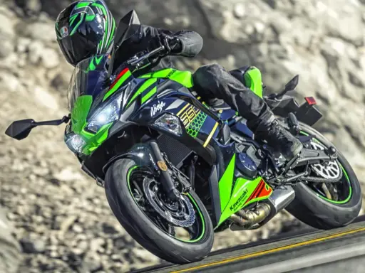 Motocyklista na zielono-czarnym Kawasaki Ninja 650, z widocznymi danymi technicznymi, pokonuje zakręt na górskiej drodze.