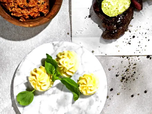 Ein Steak mit Kräuterbutter, dazu Kartoffelröschen und eine Schüssel mit einer roten Paste. Perfekt für ein knoblauchbutter rezept.