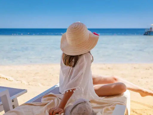 Dziewczynka w kapeluszu na plaży, marząca o tym, gdzie warto polecieć. Piękne morze i słońce zachęcają do odpoczynku.