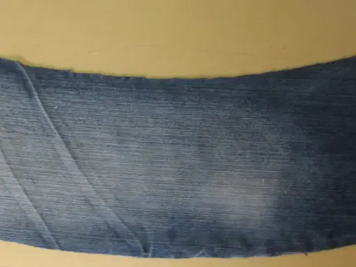 Ett utskuret jeansstycke med en vågig kant, redo att sys till en volang. Röd tråd syns längs ena sidan.