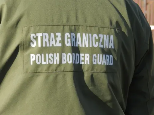 Fragment zielonego munduru Straży Granicznej z białym napisem "STRAŻ GRANICZNA POLISH BORDER GUARD".
