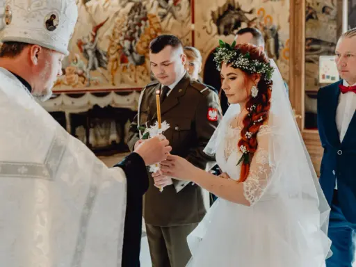 Uroczysty ślub prawosławny. Panna młoda w wianku, pan młody w mundurze, kapłan zapala świece.