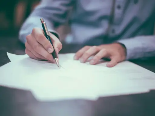 Dłoń pisze piórem na papierze, przygotowując list formalny angielski matura.