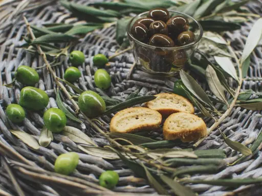 Olives vertes et noires, crostinis et feuilles d'olivier sur un panier tressé, évoquant une spécialité culinaire du Luberon.