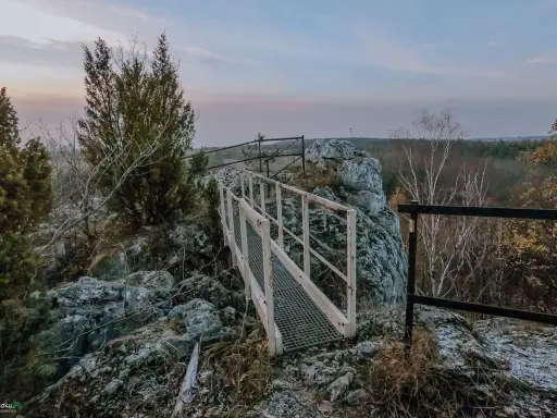 Mostek na skalnym ostańcu na Jurze Krakowskiej. W oddali las i niebo o zmierzchu.
