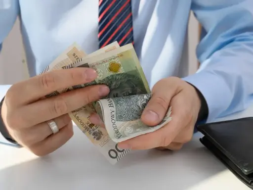 Dłonie liczą polskie banknoty. Zastanawiasz się, ile pracodawca płaci za pracownika przy najniższej krajowej?