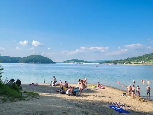 Polańczyk atrakcje: plażowicze odpoczywają nad Soliną, w tle żaglówka i zielone wzgórza.
