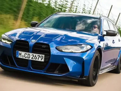 Blauer BMW M3 Competition Kombi rast auf einer Landstraße, die Sonne spiegelt sich im Lack.