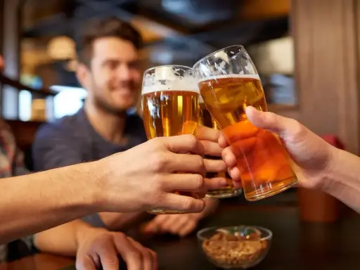 Trzech przyjaciół wznosi toast piwem. Widać ich dłonie trzymające szklanki z bursztynowym napojem, a na stole miseczkę z orzeszkami. To idealny moment, by porozmawiać o zawartości alkoholu w piwie.