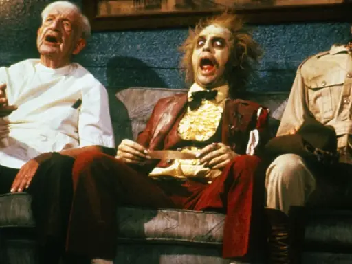 Tre personaggi bizzarri, tra cui Beetlejuice, siedono su un divano in una scena di horror comedy.