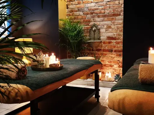 Dwie łóżka do masażu w przytulnym spa, ozdobione świecami i roślinami.