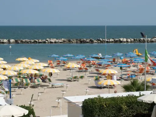 Spiaggia affollata con ombrelloni gialli e bianchi, lettini e il mare azzurro. Un'immagine di igea marittima, perfetta per una vacanza.