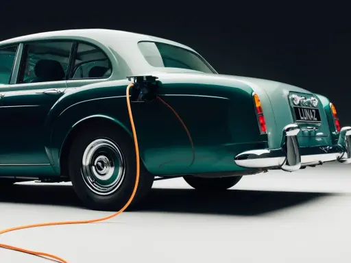 Clásico Bentley con cable de carga naranja conectado. Un ejemplo de retrofit que es la electrificación de vehículos antiguos.