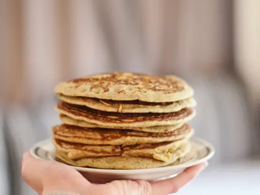 Pile de pancakes dorés à la farine de sarrasin, servis sur une assiette blanche tenue par une main.