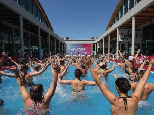 Folla entusiasta partecipa a una lezione di acquagym all'aperto, con le braccia alzate, durante la fiera dello sport Rimini.