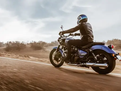 Motocyklista w skórzanej kurtce pędzi na niebieskim **super meteor 650** przez pustynny krajobraz.