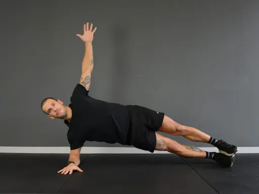 Uomo in posizione di side plank, con un braccio sollevato e l'altro appoggiato a terra.