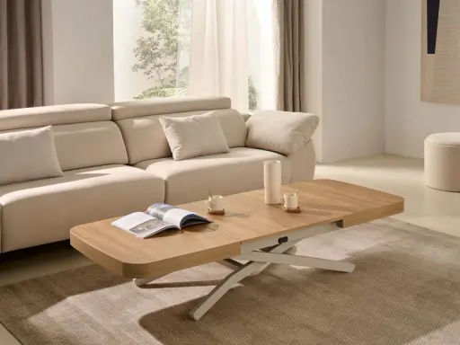 Mesa centro elevable 120x70 de madera clara, con un libro abierto y taza de café, junto a un sofá beige en un salón luminoso.