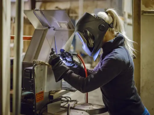 Kobieta w masce spawalniczej wykonuje spawanie w domu. Precyzyjnie łączy metalowe elementy, tworząc coś nowego.