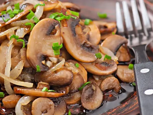 Jak usmażyć pieczarki? Na talerzu aromatyczne, podsmażone pieczarki z cebulką i szczypiorkiem, gotowe do jedzenia.