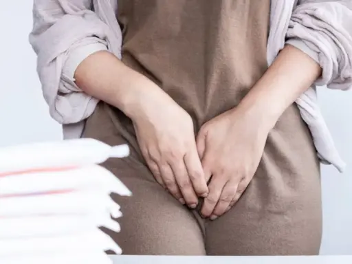 Kobieta zakrywa dłoniemi okolice intymne, obok stos podpasek. Może to sugerować problem z wydzieliną z pochwy.