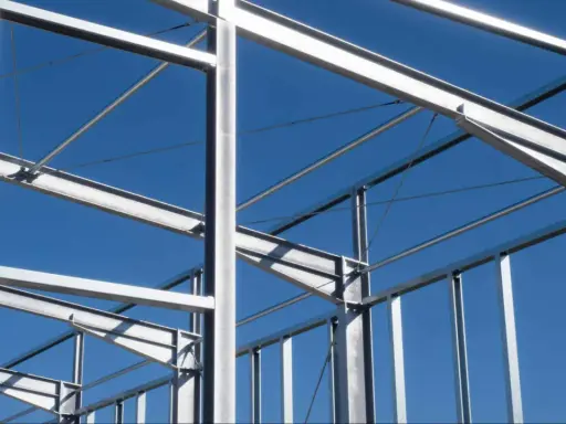 Structure métallique d'un bâtiment en construction, avec des poutres et des poteaux d'acier sous un ciel bleu clair.