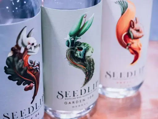 Drei Flaschen Seedlip alkoholfreien Gin mit kunstvollen Etiketten, die fantasievolle Tiere und Pflanzen zeigen.