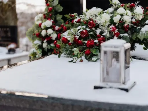 Wieniec dla taty: czerwone róże i białe kwiaty na śniegu, obok lampion.