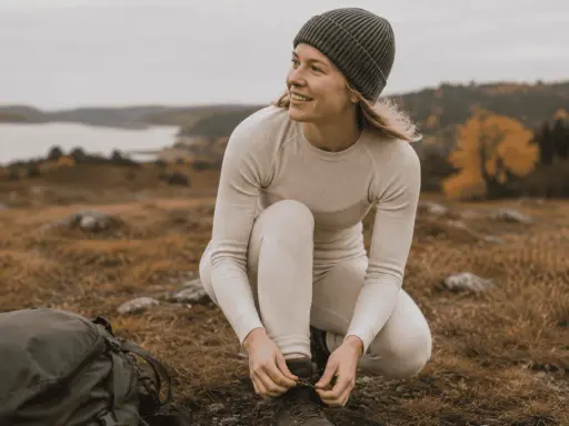Kvinna i viskos svett-underställ knyter kängor i svensk natur.