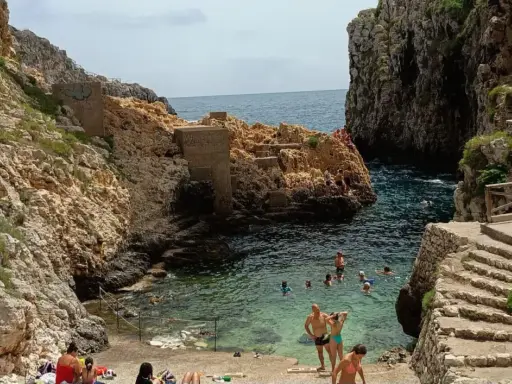 Santa Maria di Leuca: cosa vedere? Una caletta rocciosa con gente che nuota e si rilassa, con scalinate di pietra che scendono verso il mare cristallino.