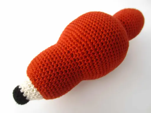 Un adorable zorro amigurumi de lana naranja, con detalles blancos y negros en el hocico, listo para jugar.
