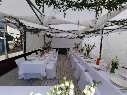 Elegancka komunia w namiocie. Białe obrusy, kwiaty i szklane lampiony tworzą uroczystą atmosferę.