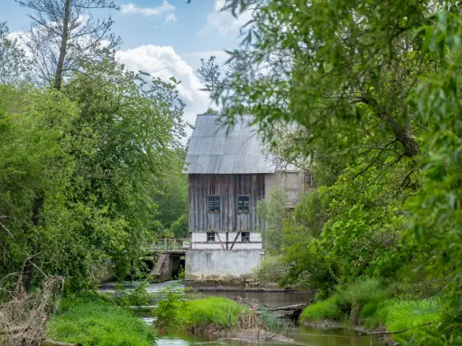 Stary młyn nad rzeką w Bolimowskim Parku Krajobrazowym, otoczony bujną zielenią.