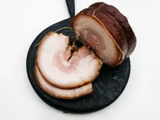 Pokrojony boczek chashu, z widocznymi warstwami mięsa i tłuszczu, ułożony na ciemnej desce.
