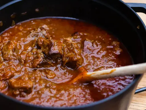 Ein dampfender Topf mit zartem Wiener Saftgulasch, das mit einer Holzschaufel umgerührt wird.