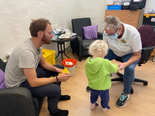 En pappa och ett barn får vaccin av en sjuksköterska. Barnet verkar lite oroligt, men sjuksköterskan är lugn och trygg. Det är en fin stund av vaccin italien.