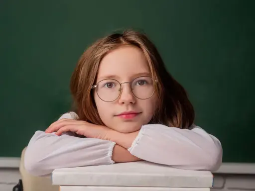 Dziewczynka w okularach opiera głowę na stosie książek. Zastanawia się, do kiedy można pobierać zasiłek rodzinny.
