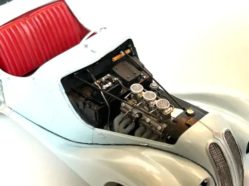 Detailansicht eines Modellautos mit rotem Lederinterieur und detailliertem Motor, dessen Teile mit Chromfolie veredelt sind.