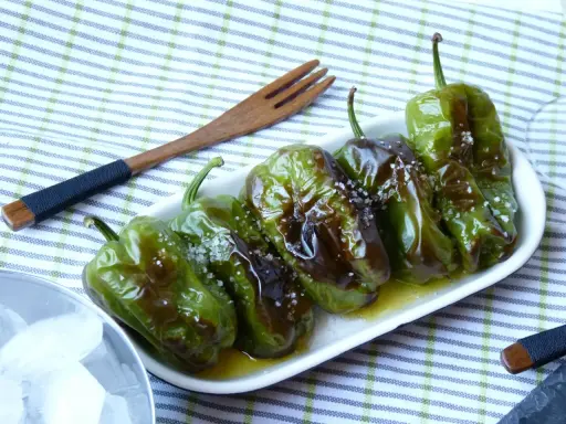 Délicieux **pieds de poivrons** verts, grillés et saupoudrés de gros sel, servis dans une assiette blanche avec une fourchette en bois.